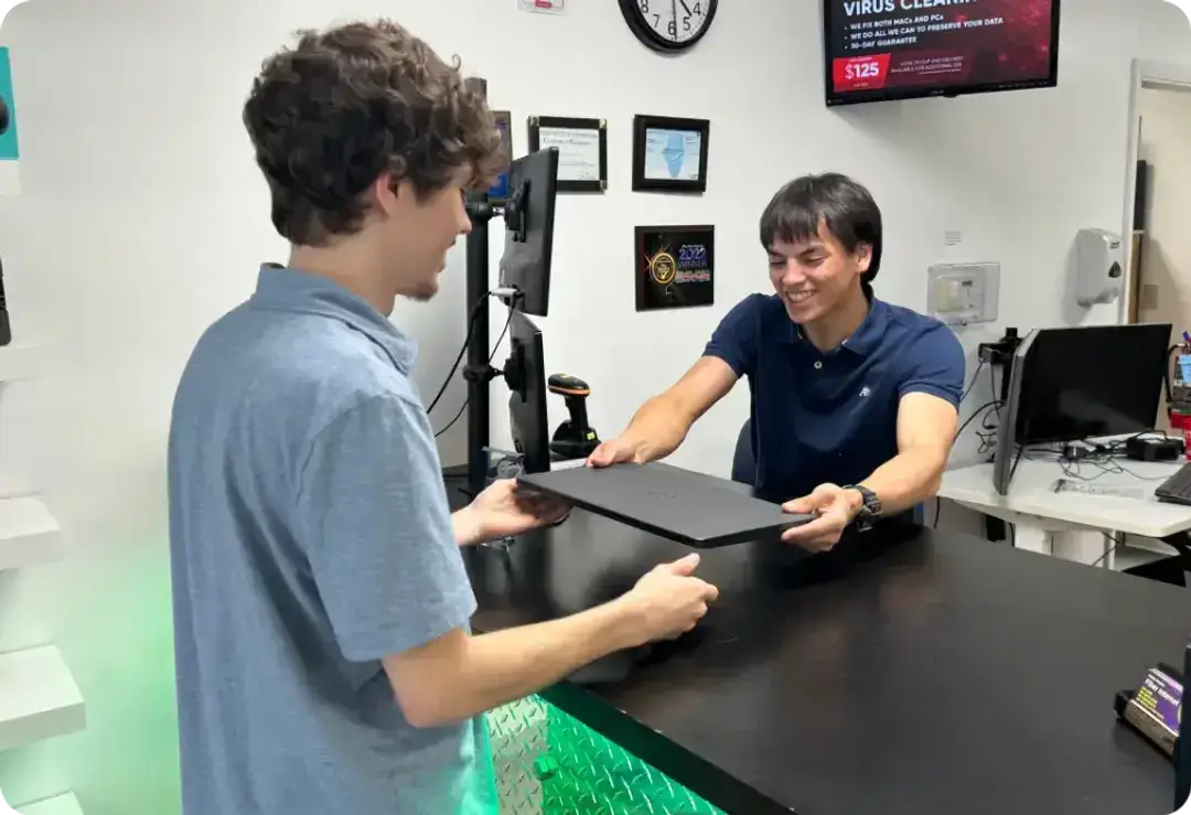 A friendly sales associate at Simplified Computers hands a repaired computer back to a happy customer — representing expert IT support, repair service, and PC repair in Champaign offered by this trusted IT Champaign provider.